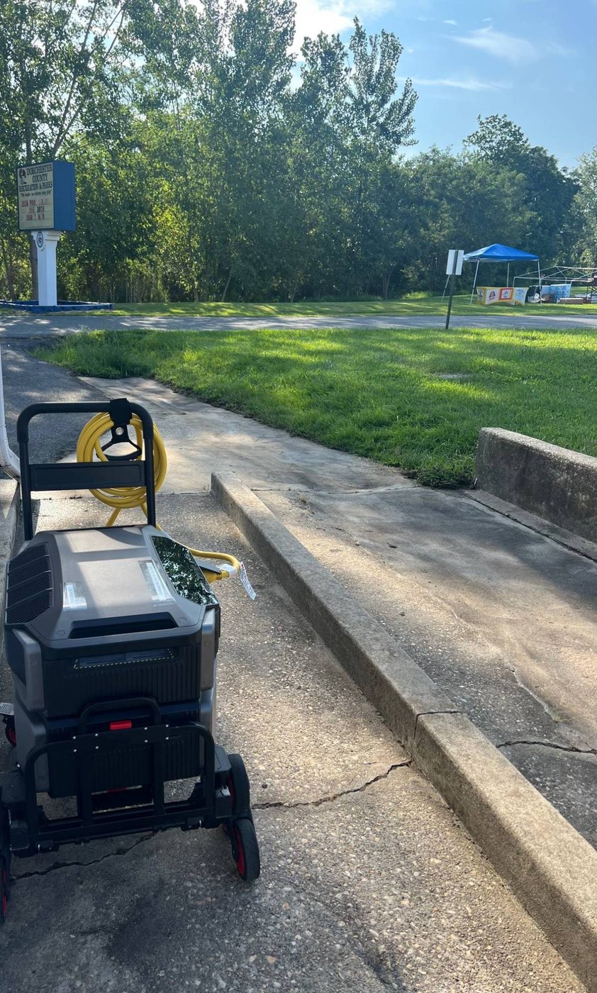 EcoFlow rig with a coiled 50-amp cable on a wheeled cart, parked on a park sidewalk with vendor tents visible in the distance